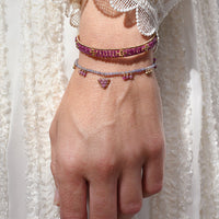 Hand wearing multiple bracelets with a white lace garment in the background