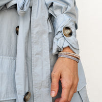 Close-up of a light blue gray coat with buttons and a person's arm wearing a stack of tanzanite bracelets.