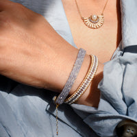Close-up of a person wearing a gold necklace and bracelets on a light blue fabric background