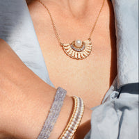 Close-up of a person wearing a gold necklace and bracelets on a light blue fabric background