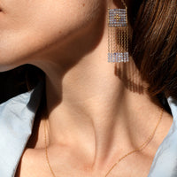 Close-up of a person wearing gold earrings and a necklace with a light blue shirt.