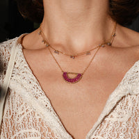 Close-up of a woman wearing a delicate gold and red gemstone necklace with a lace top.