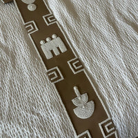 A close-up of a textured cream-colored fabric, likely a quilt or bedspread, featuring a decorative brown vertical band with white geometric and stylized animal motifs.