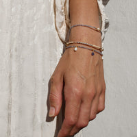 Hand wearing multiple bracelets on a textured light background