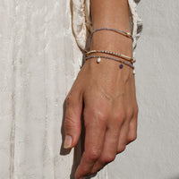 Hand wearing multiple tanzanite bracelets on a textured light background