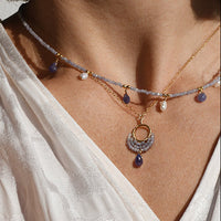 Close-up of a person wearing multiple necklaces and bracelets on a light background