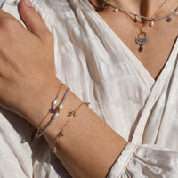 Close-up of a person wearing multiple necklaces and bracelets on a light background
