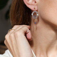 Close-up of a person wearing a circular earring with tanzanite blue stones and a gold ring.