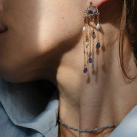Close-up of a person wearing a dangling chandelier type earring with pearls and Tanzanite gemstones.