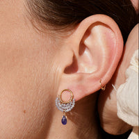 Close-up of a woman wearing gold stud earrings with a blue purple tanzanite gemstone.