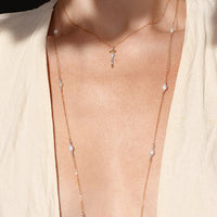 Person wearing a beige top with a necklace, standing outdoors.
