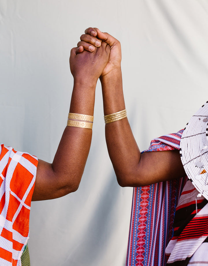 Ladies holding hands, wearing traditional clothing, gold bangles and Maasai beaded discs.