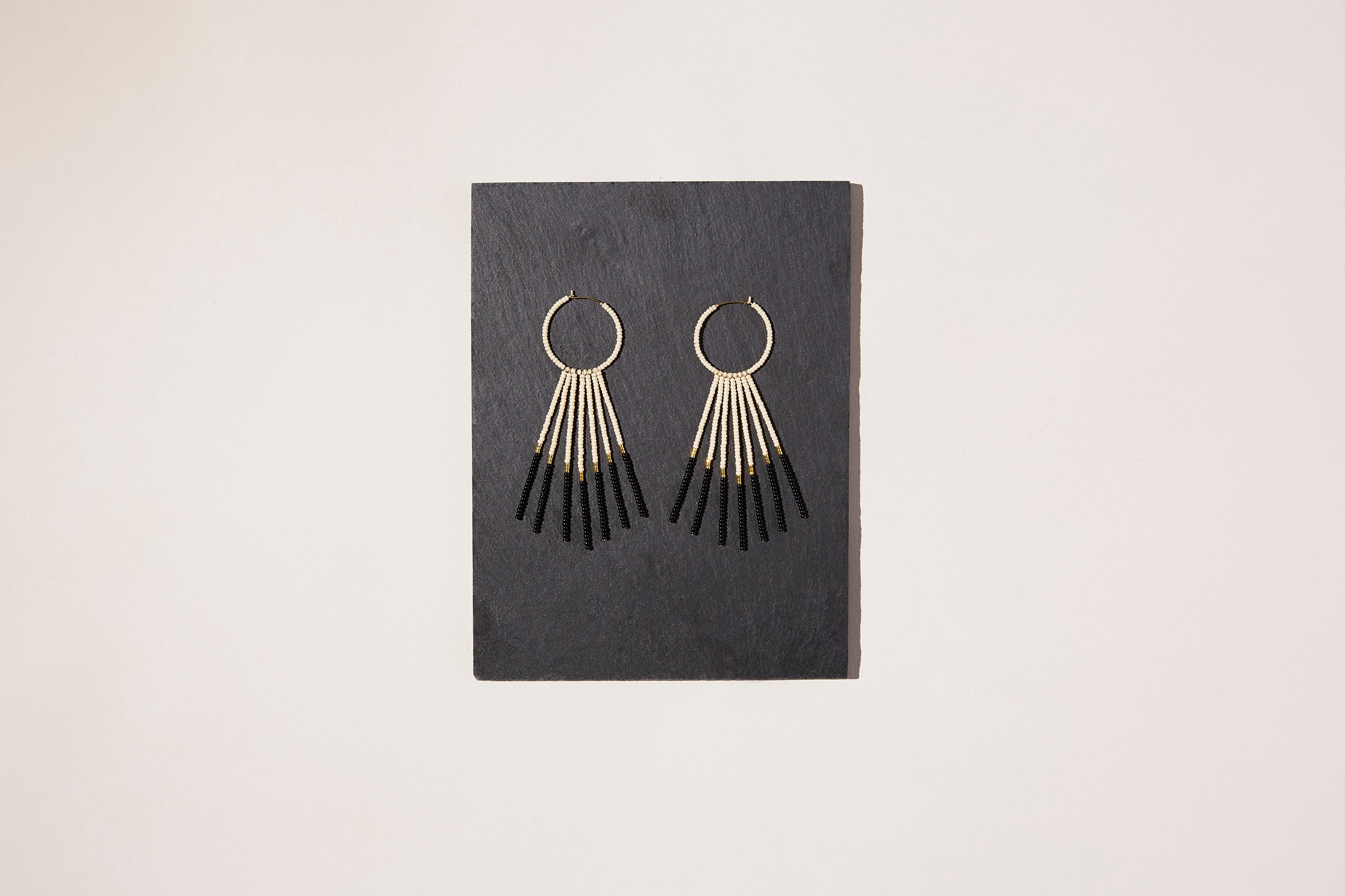 Pink black and gold statement beaded hoop drop earrings on a piece of slate.