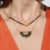 Close-up of a person wearing an orange top with a necklace and earrings.