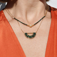 Close-up of a person wearing an orange top with a necklace and earrings.