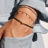 Person wearing a light gray outfit with a bracelet on a neutral background