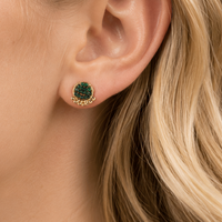 Close-up of a woman's ear wearing green gemstone earrings with gold settings.