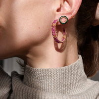 Close-up of a person wearing colorful hoop earrings with a neutral background