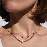Close-up of a person wearing a necklace and earrings with a neutral background