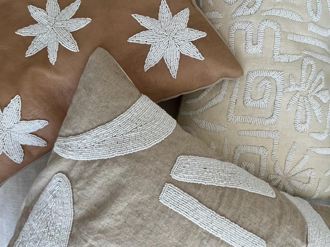 Three decorative throw pillows with intricate white embroidered patterns, including starbursts and abstract geometric designs, arranged together on a neutral surface.