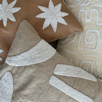 Three decorative throw pillows with intricate white embroidered patterns, including starbursts and abstract geometric designs, arranged together on a neutral surface.