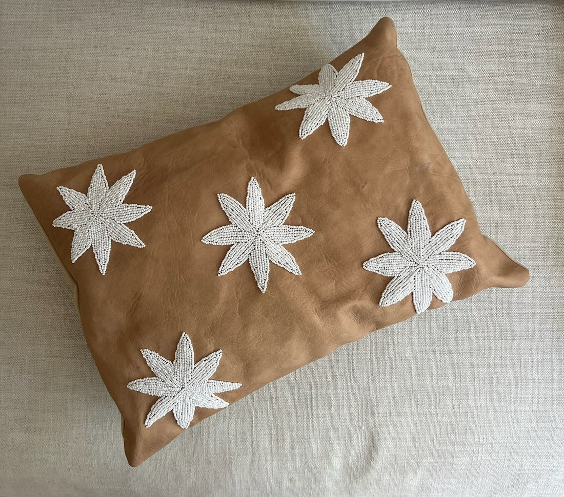 A rectangular tan cushion with five white embroidered starburst motifs, resting on a light beige textured sofa.