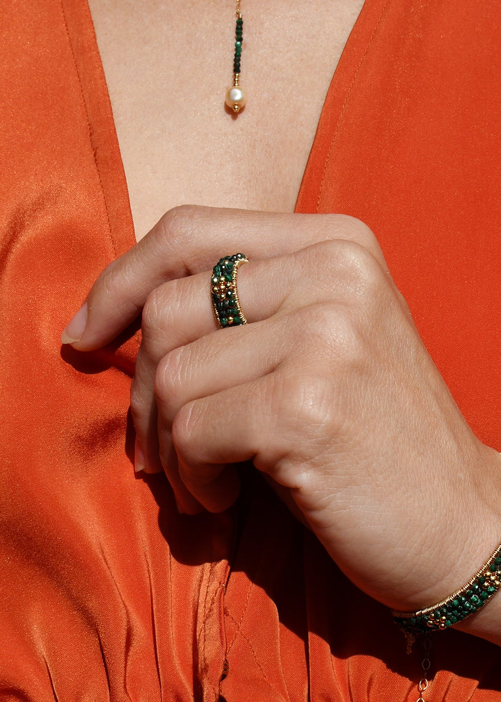 Person wearing an orange outfit with a green beaded bracelet and ring.