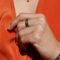 Person wearing an orange outfit with a green beaded bracelet and ring.