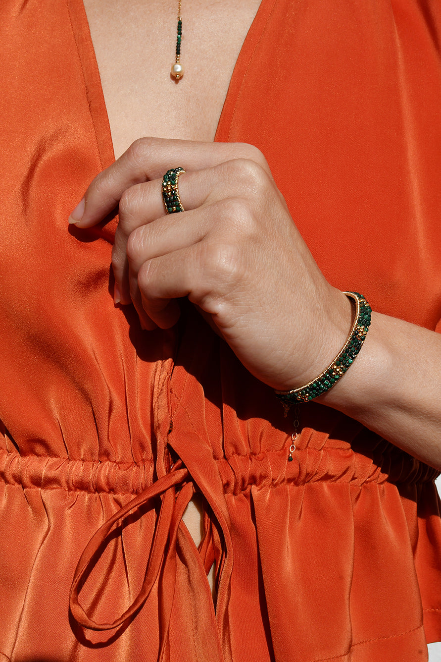 Person wearing an orange outfit with a green beaded bracelet and ring.