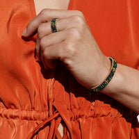 Person wearing an orange outfit with a green beaded bracelet and ring.