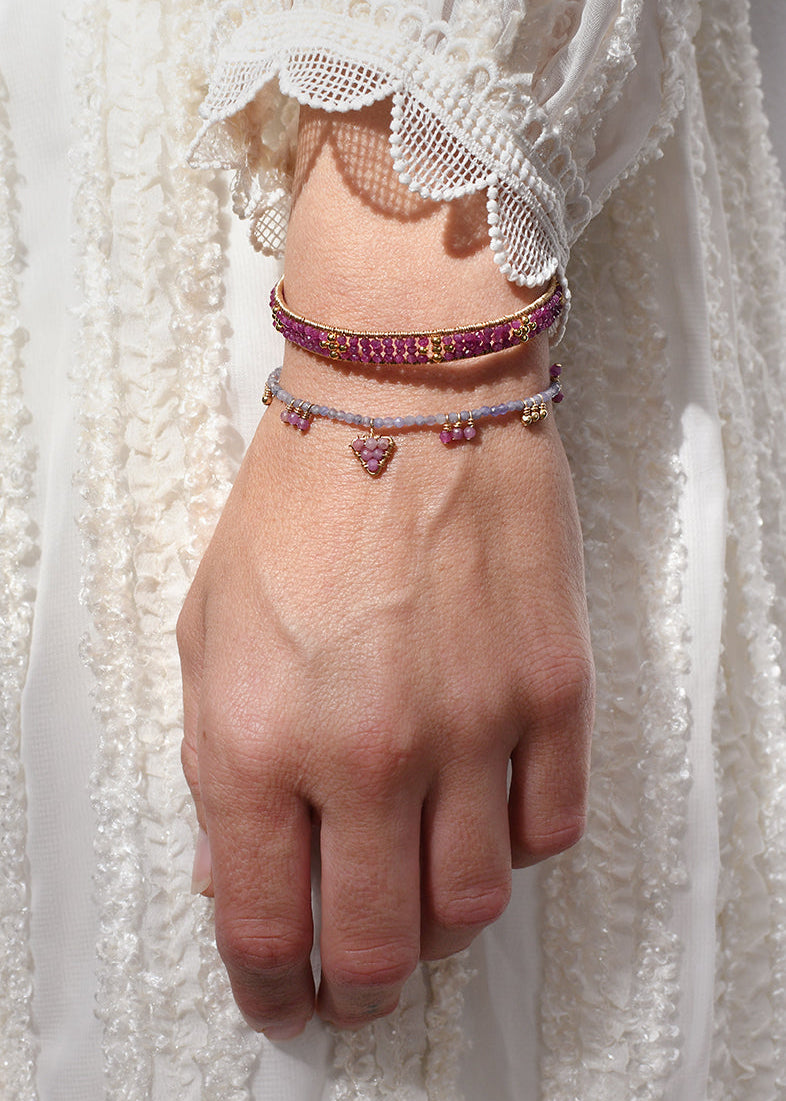 Hand wearing multiple bracelets with a white lace garment in the background