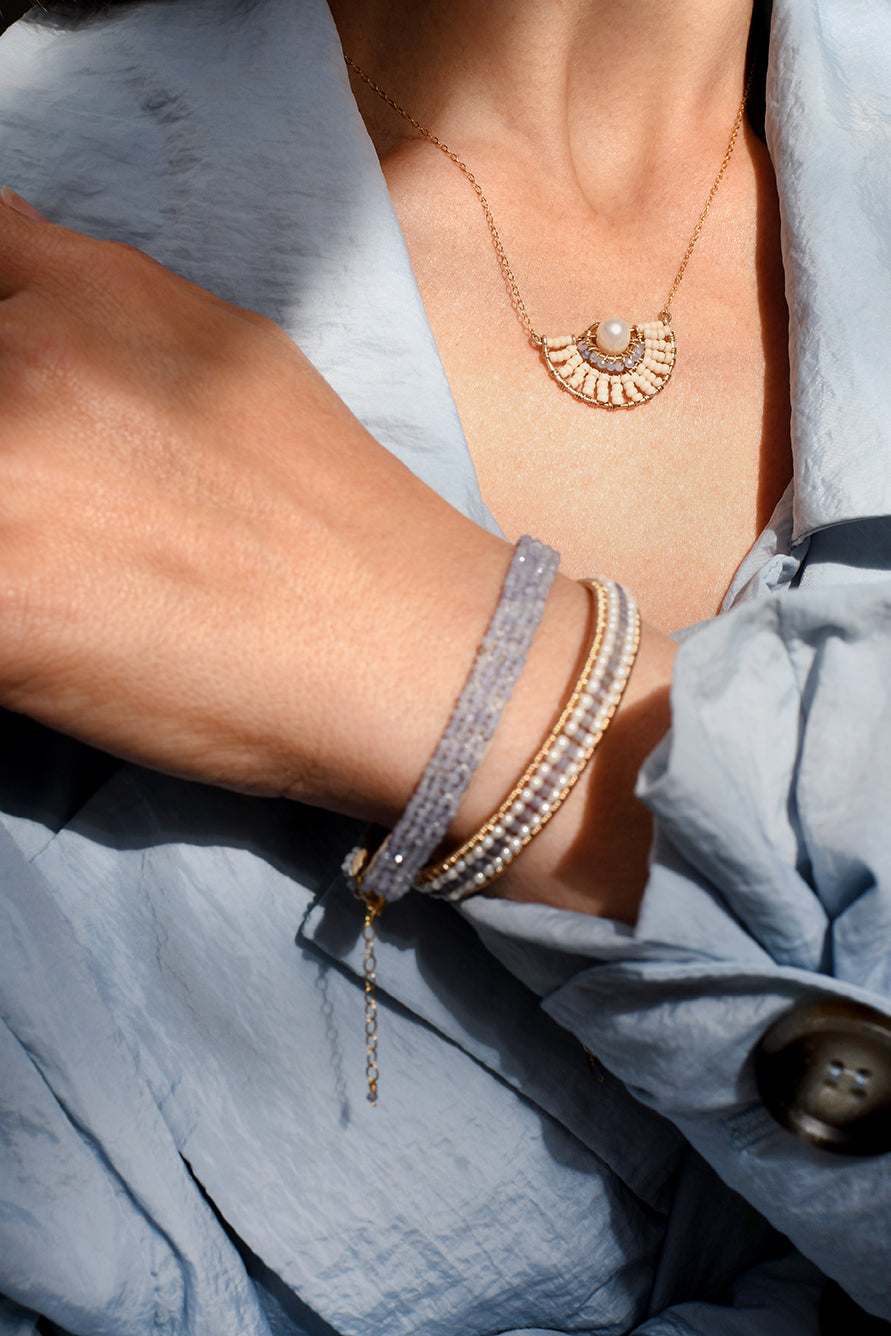 Close-up of a person wearing a gold necklace and bracelets on a light blue fabric background
