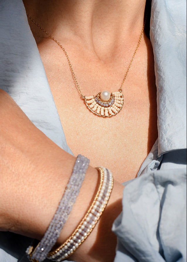 Close-up of a person wearing a gold necklace and bracelets on a light blue fabric background