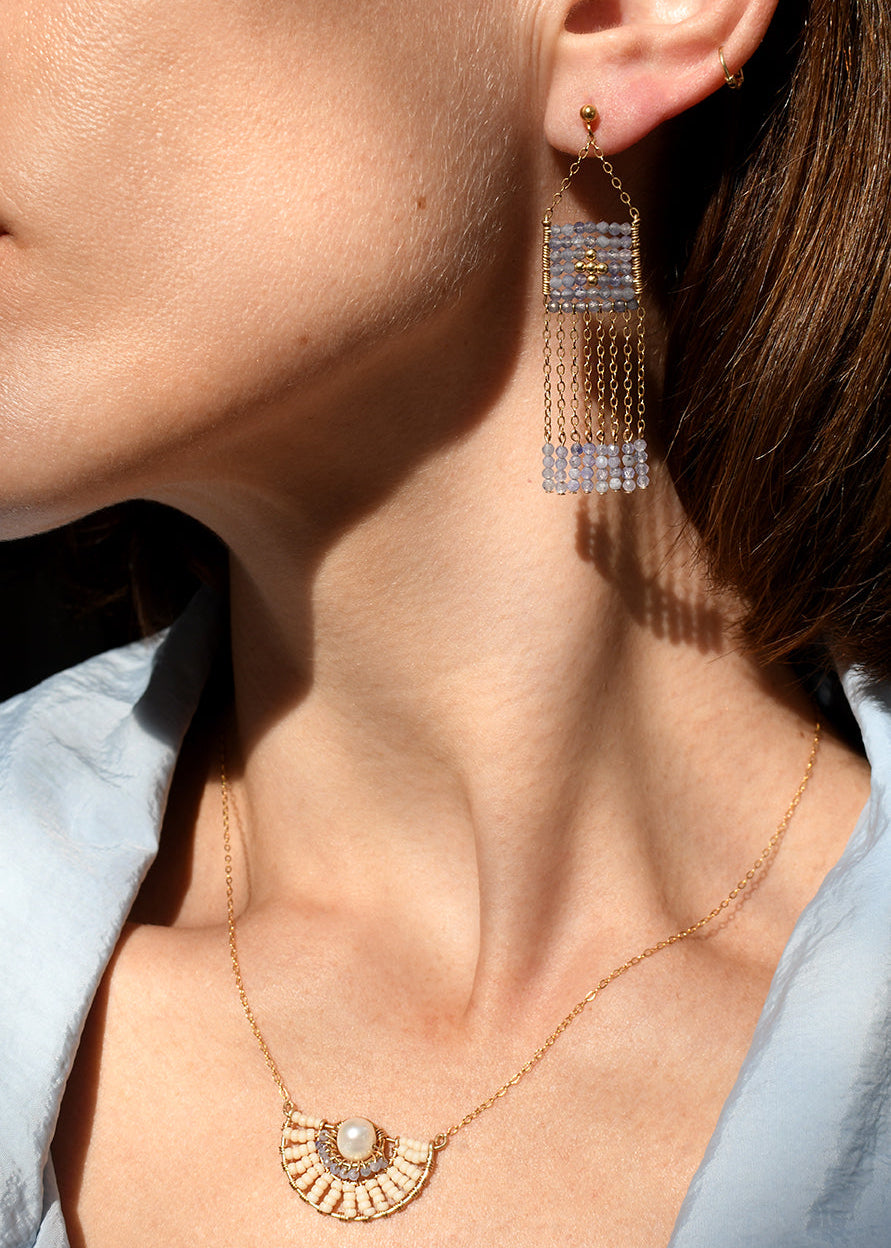 Close-up of a person wearing gold earrings and a necklace with a light blue shirt.
