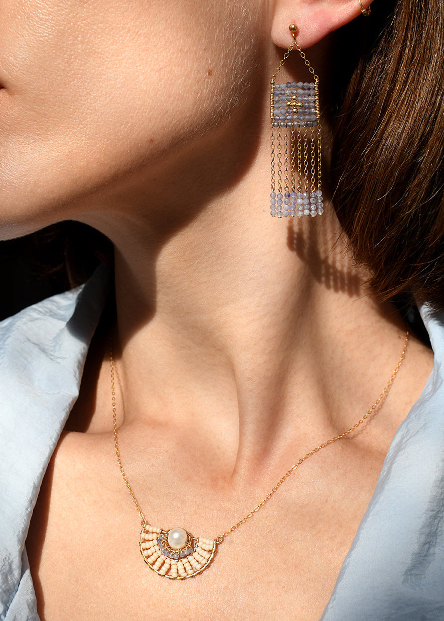 Close-up of a person wearing gold earrings and a necklace with a light blue shirt.