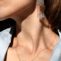 Close-up of a person wearing gold earrings and a necklace with a light blue shirt.