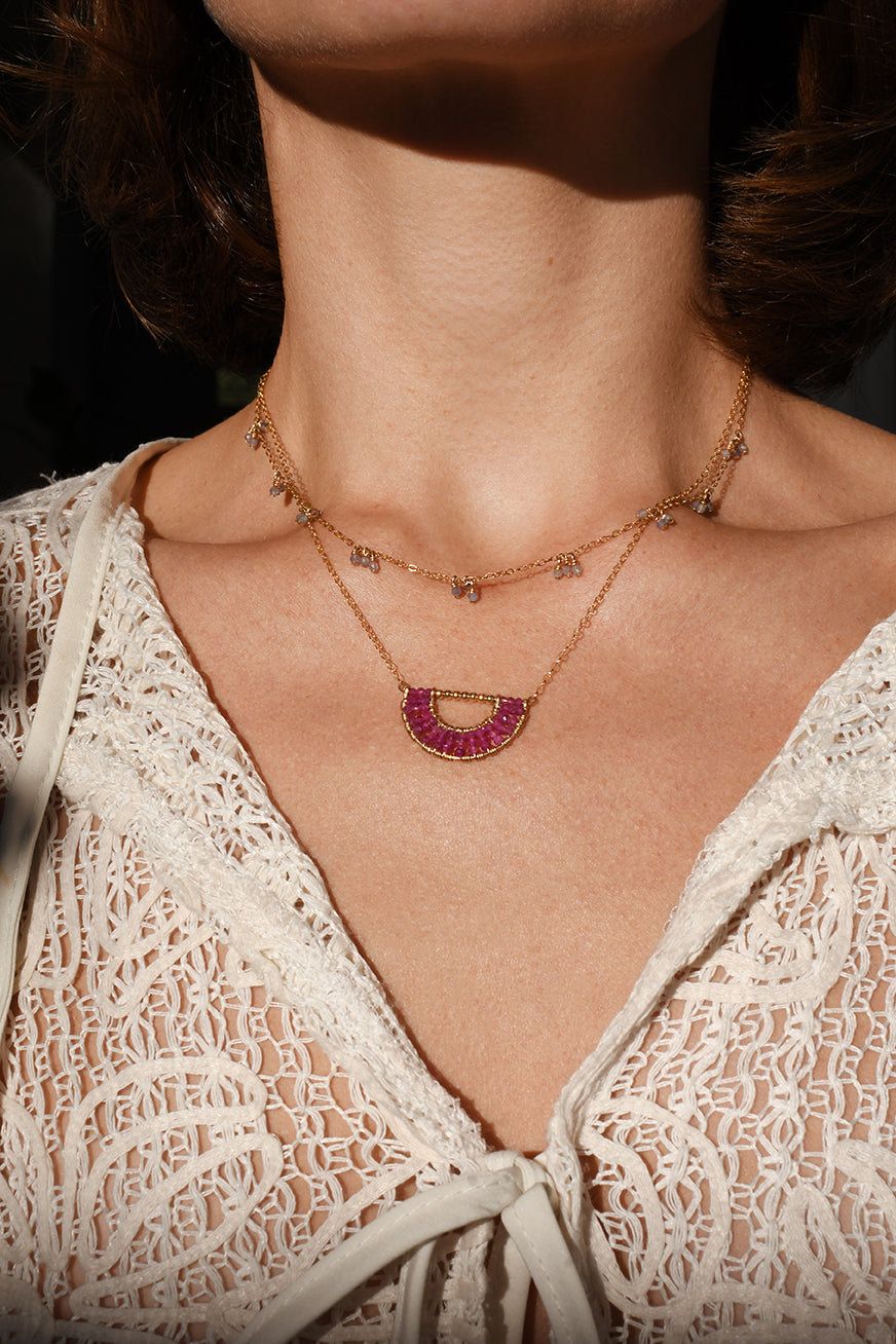 Close-up of a woman wearing a delicate gold and red gemstone necklace with a lace top.