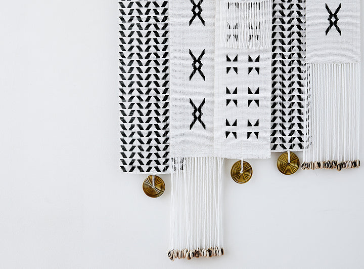 Assorted monochromatic modern African beaded decorative wall hangings with geometric shapes, traditional Maasai brass coils and shells.