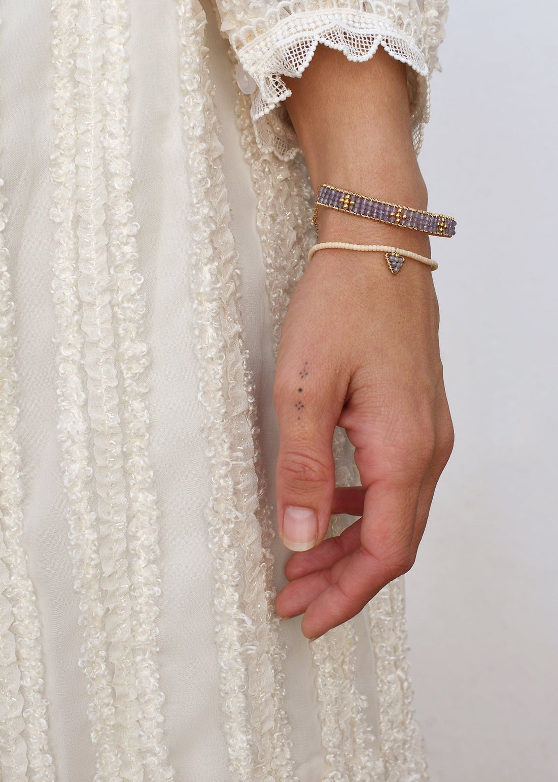 Hand wearing multiple bracelets with a white lace garment in the background