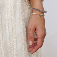 Hand wearing multiple bracelets with a white lace garment in the background