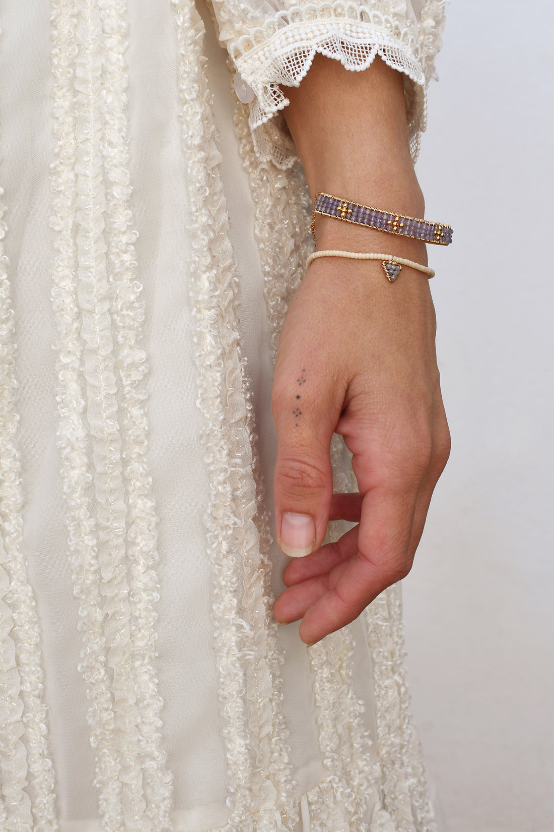 Hand wearing multiple bracelets with a white lace garment in the background