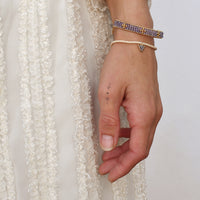 Hand wearing multiple bracelets with a white lace garment in the background