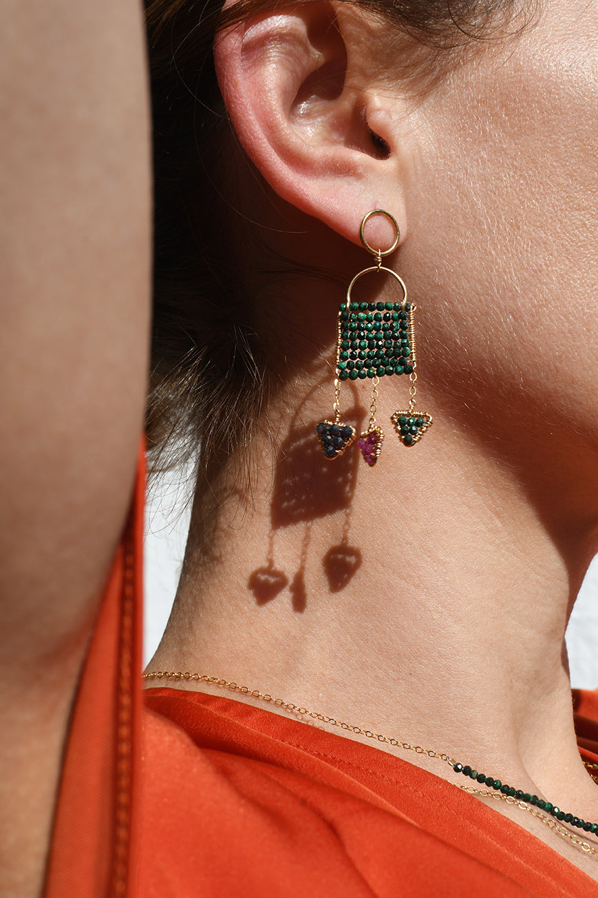 Close-up of an earring with green gemstones on a person wearing an orange top.