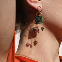 Close-up of an earring with green gemstones on a person wearing an orange top.