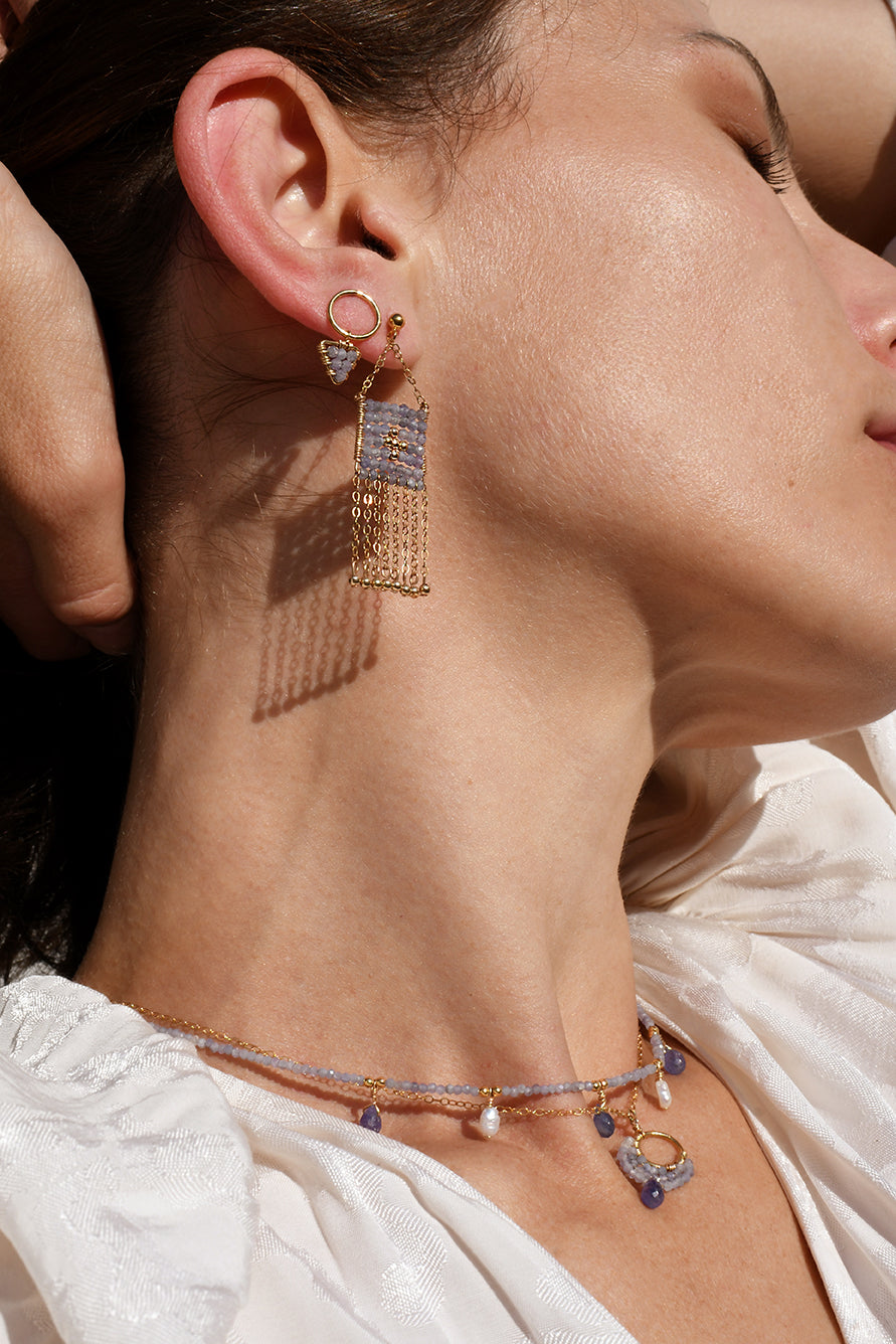 Close-up of a woman wearing gold fringe earrings and a delicate necklace.