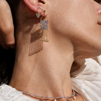 Close-up of a woman wearing gold fringe earrings and a delicate necklace.