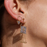 Close-up of a woman wearing gold fringe earrings and a delicate necklace.
