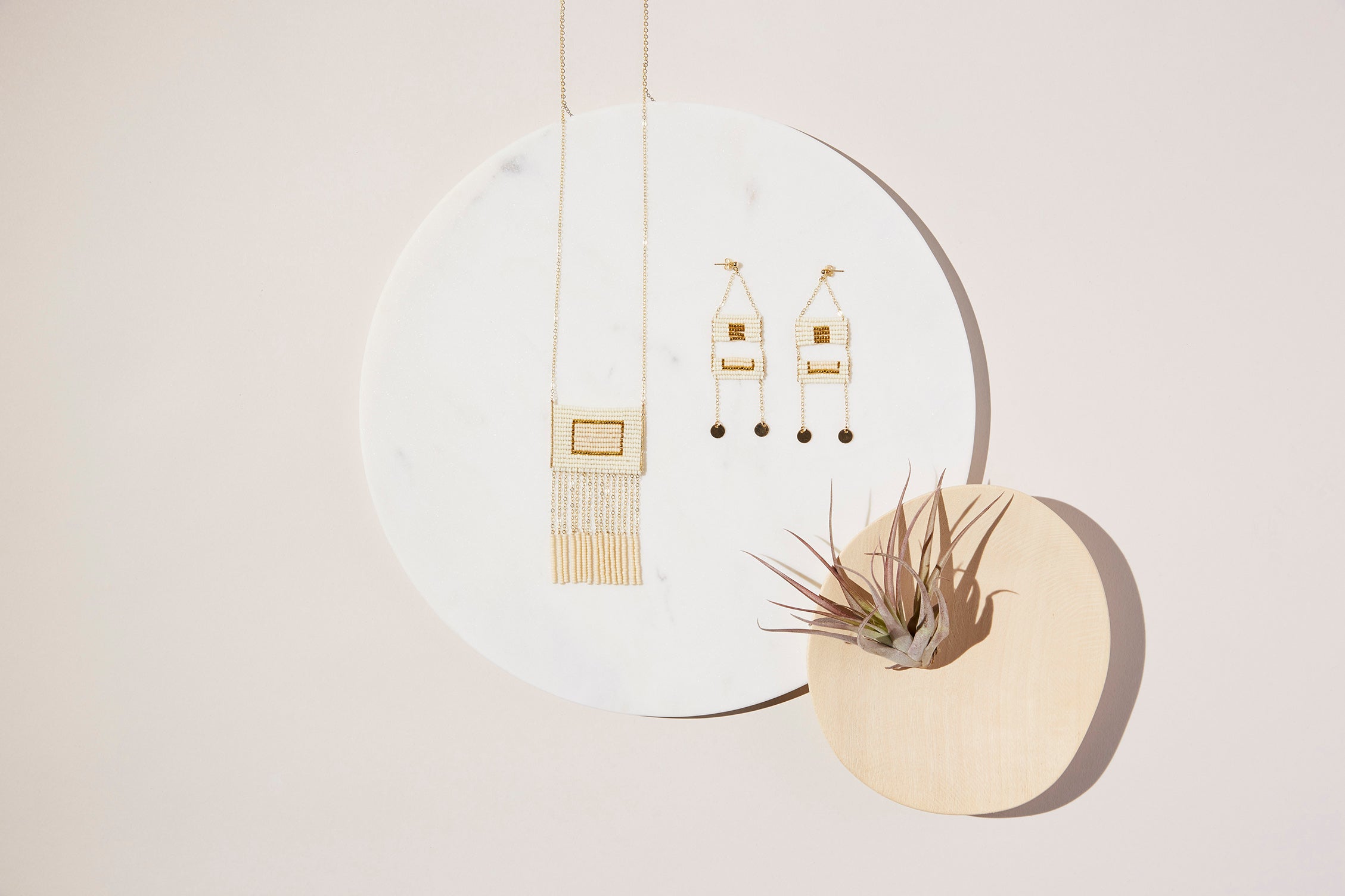 Modern African inspired hand beaded necklace with 14kt gold filled tassels and Maasai inspired fine stud earrings with gold disks sitting on a marble disk.