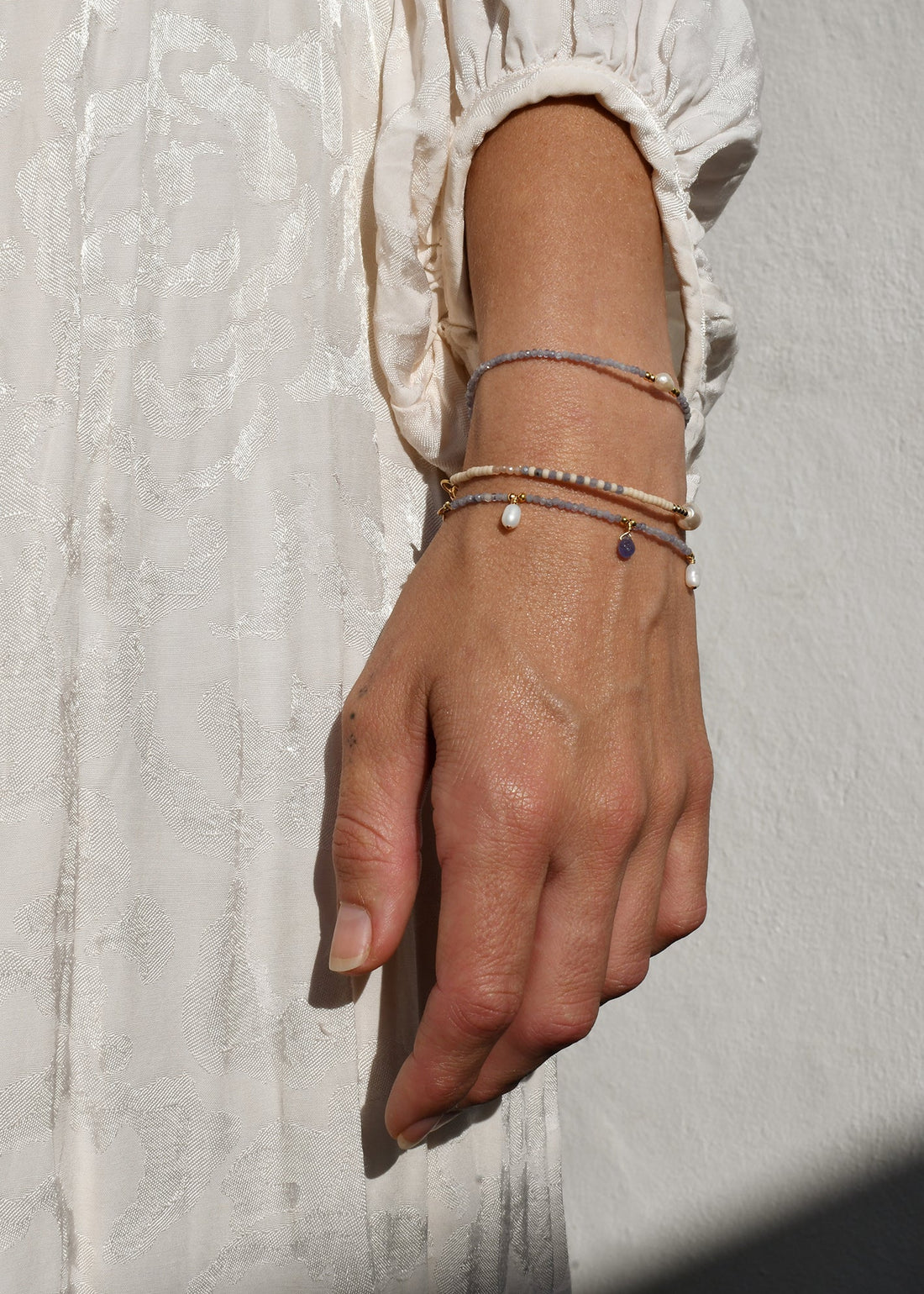 Hand wearing multiple bracelets on a textured light background