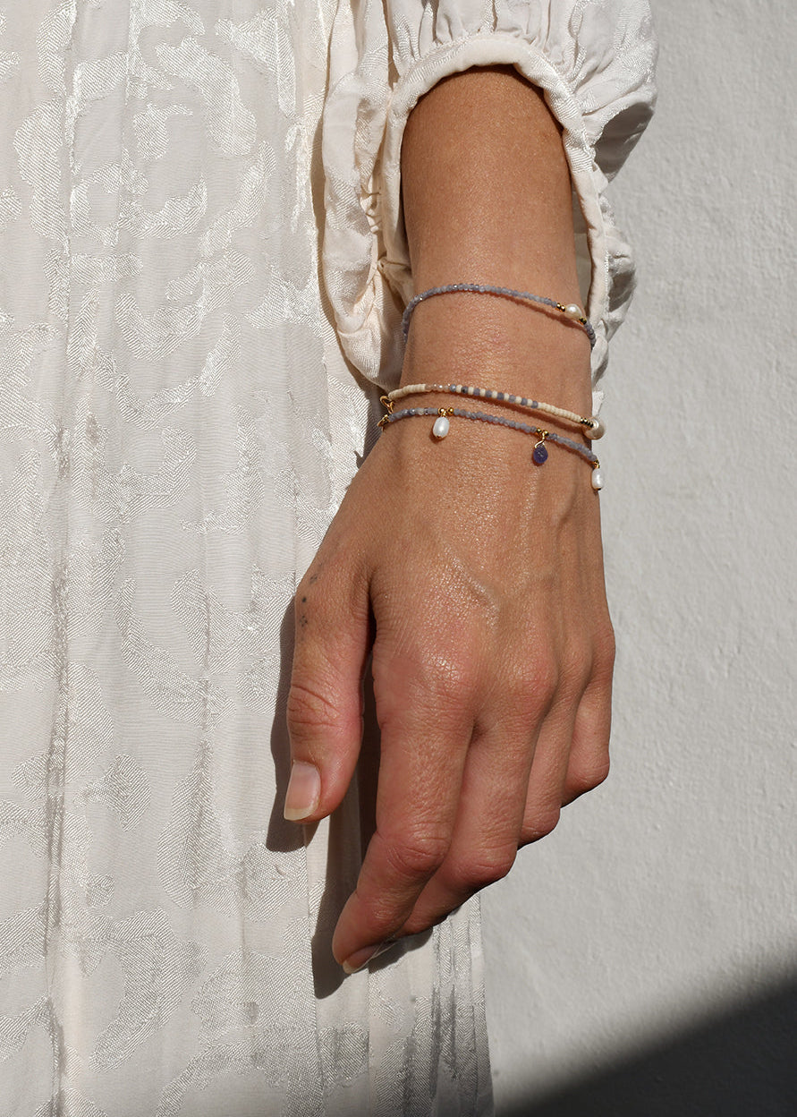 Hand wearing multiple tanzanite bracelets on a textured light background